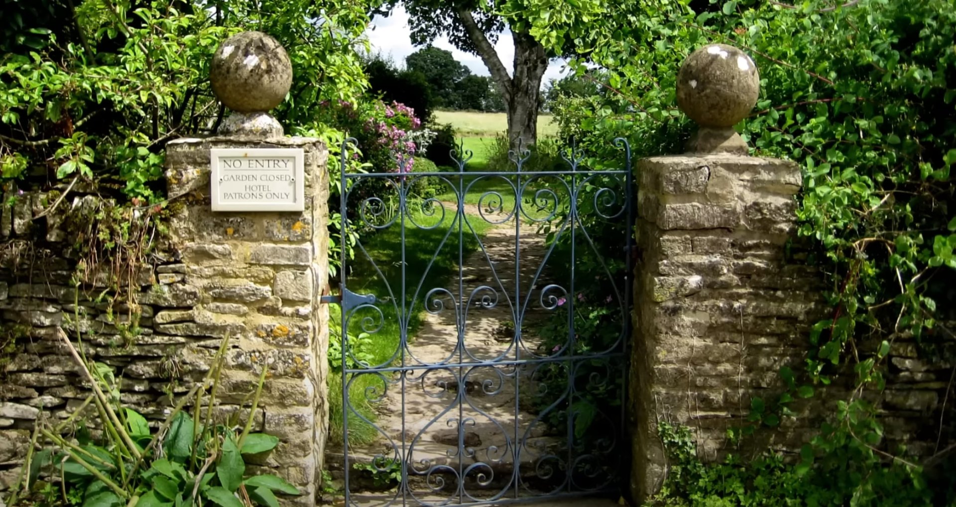 Professional landscape design featuring stone entrance and mature garden Elegant stone garden gate with professional landscaping and mature trees